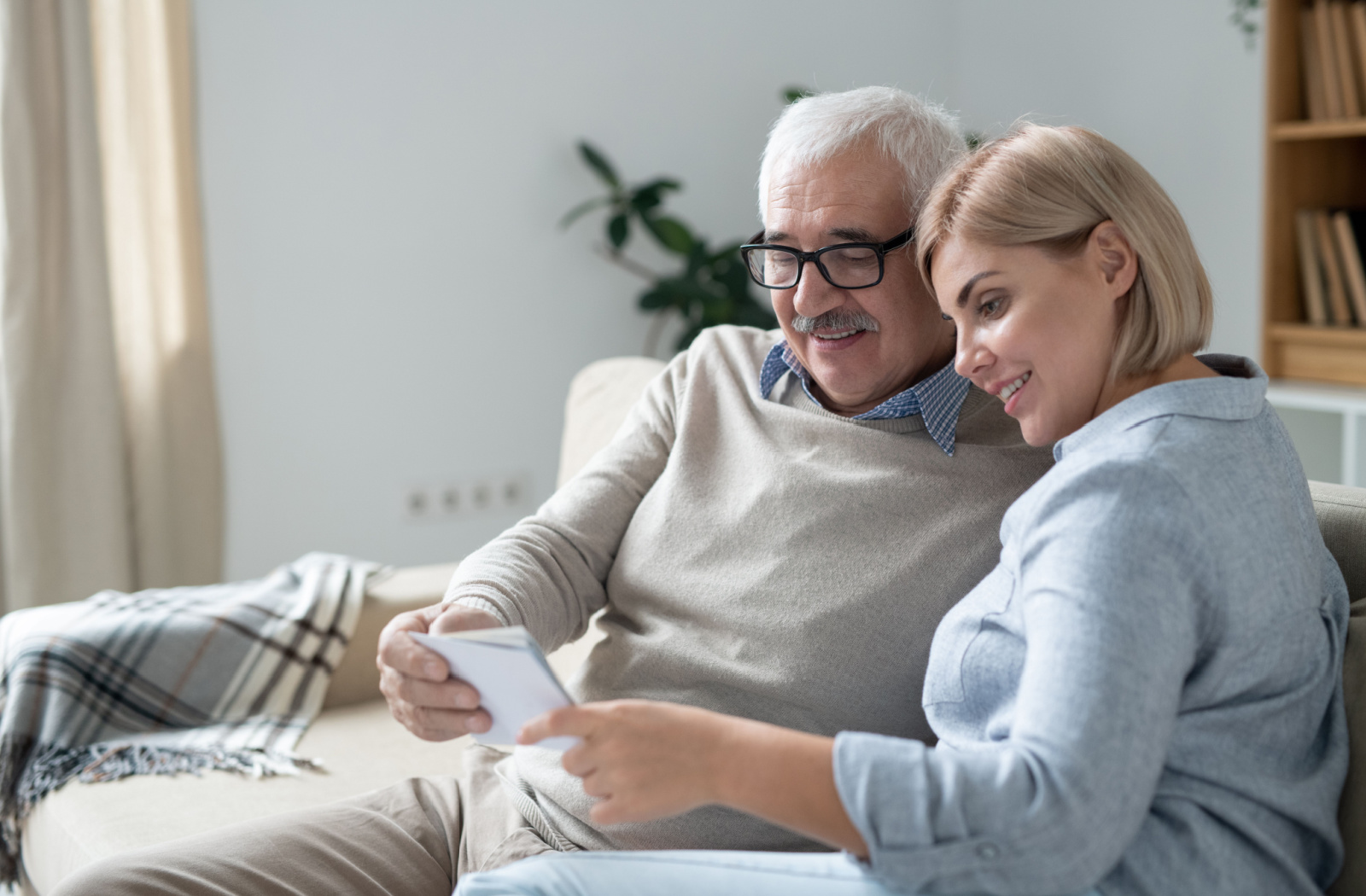 A senior man and his young daughter looking at one of their family pictures while relaxing on the couch in the living room.