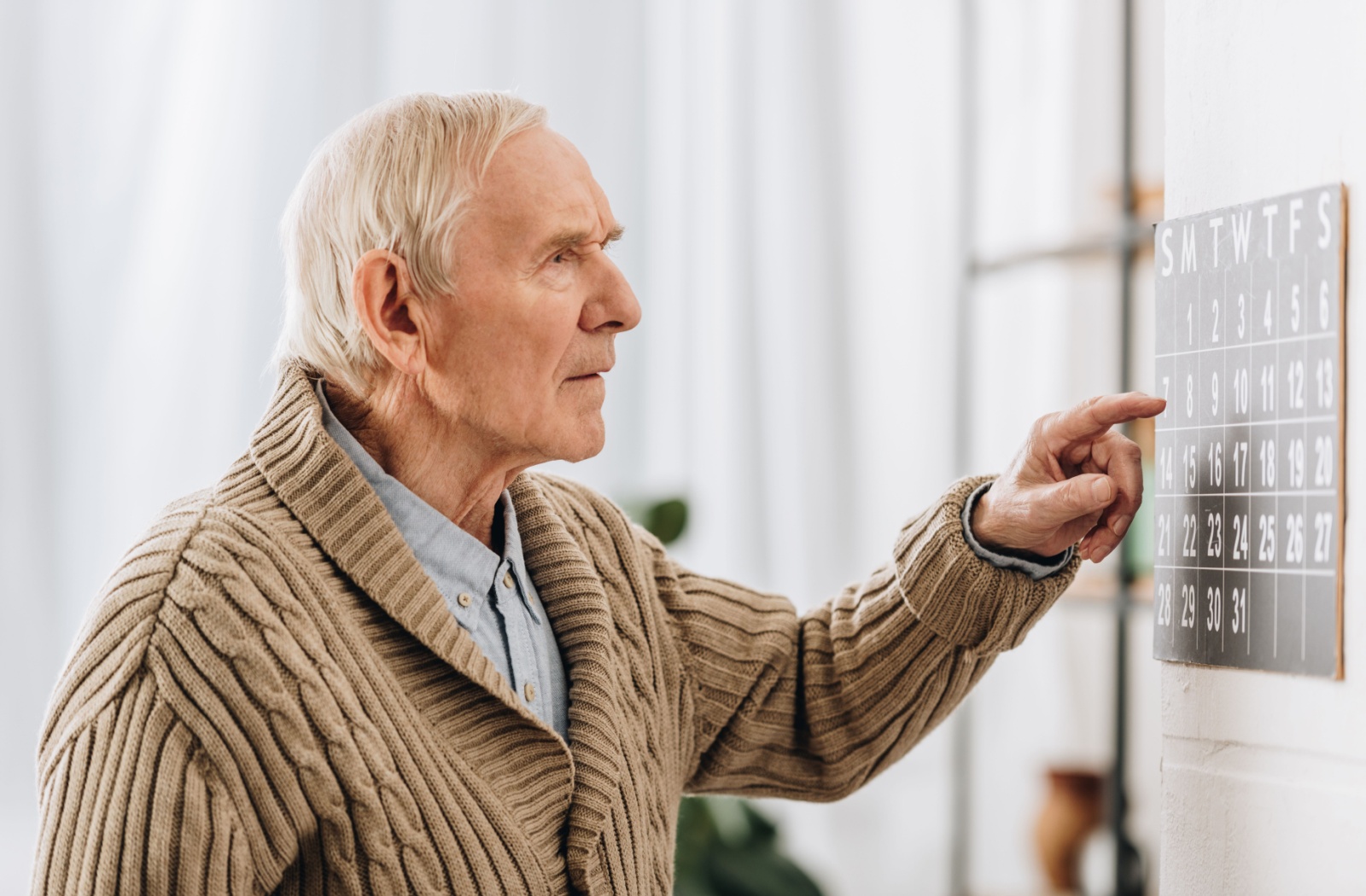 An older adult man with a forgetful-look looking at a calendar.