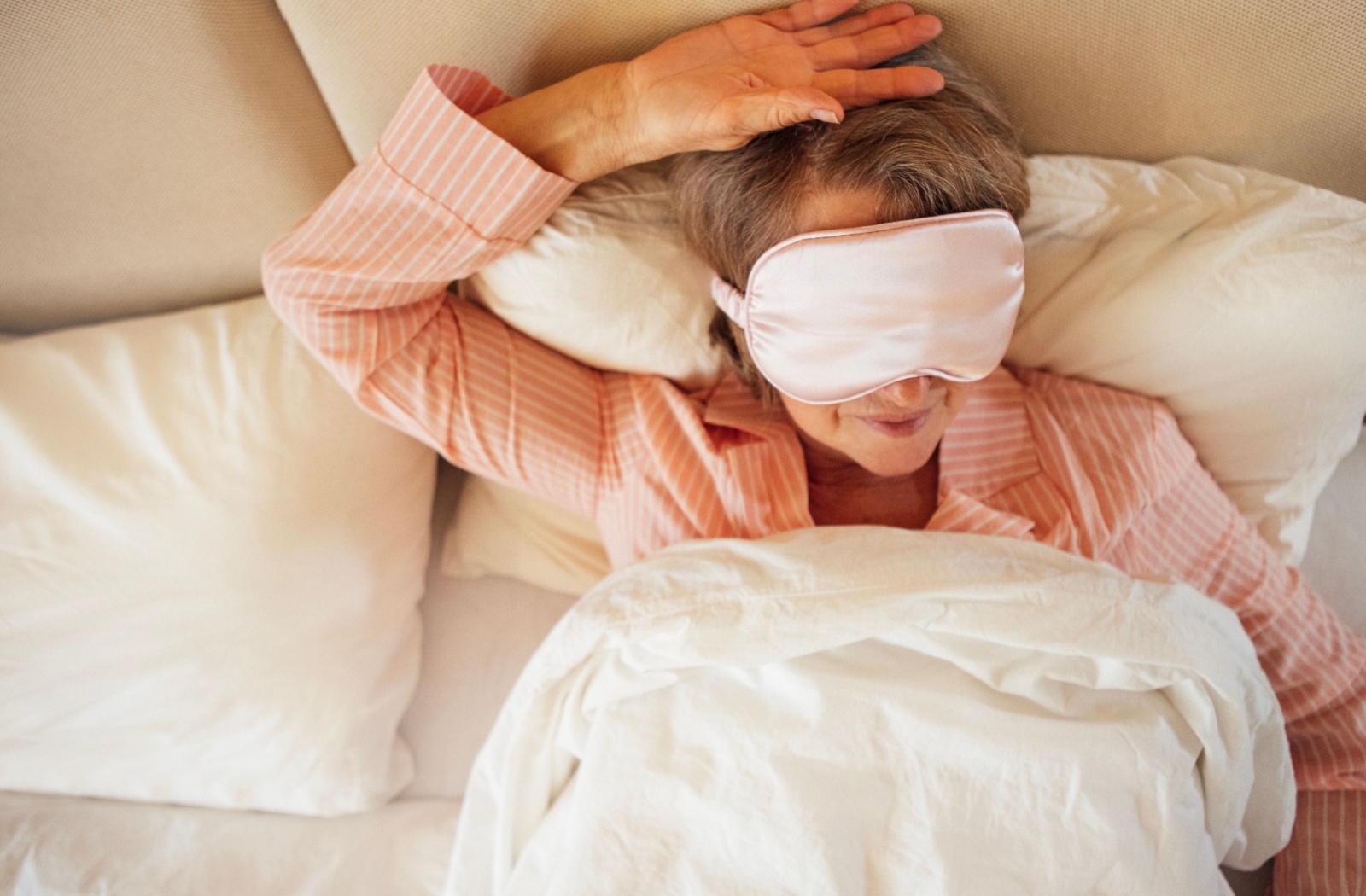 Senior wearing pink sleep mask resting peacefully in bed during relaxed morning routine
