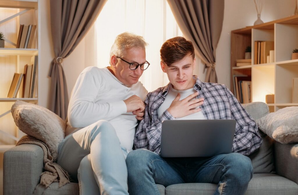 An adult and their senior parent are on a laptop together, researching the benefits of senior living communities.