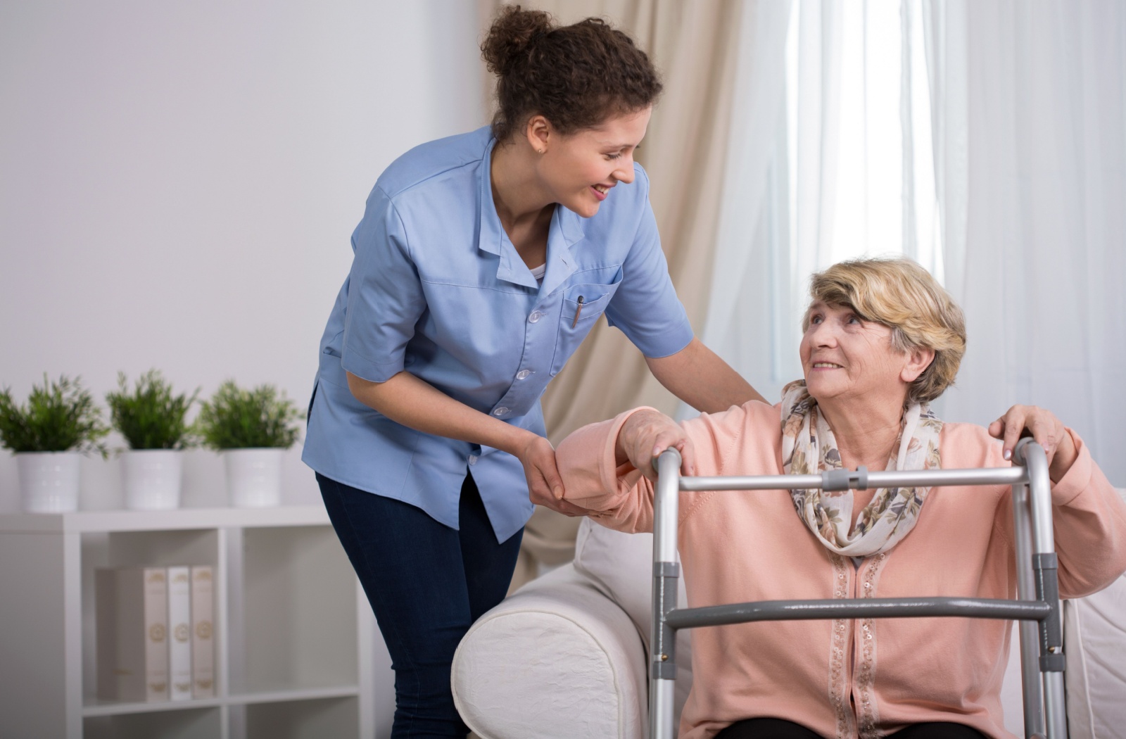 A nurse happily assists a senior in getting out of a chair with the aid of a walker after a hip fracture