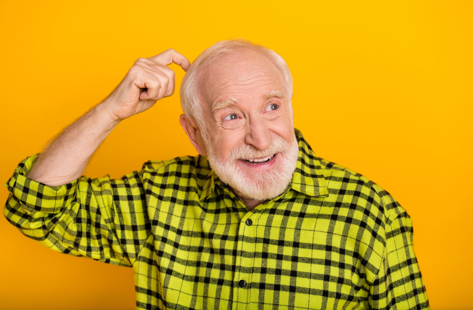 Against a yellow background, a senior in plaid playfully scratches their head as a result of forgetting something